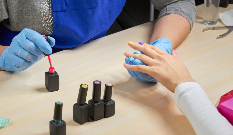 Woman having nail manicure in beauty salon. Manicurist holding hands of the client in beauty salon on desktop for manicure with nail polishes, napkins and instruments.